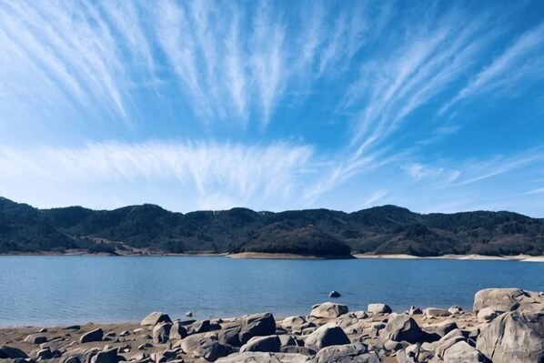 A rocky shoreline with a calm body of water and distant hills. - papaWO Homestay (Hangzhou)