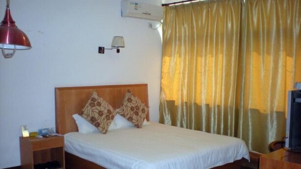 A hotel room with a wooden bed, a nightstand, a lamp, and a television.