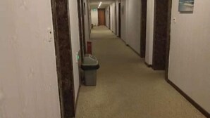 A hotel hallway with carpeted floors, doors on both sides, and a trash bin in the center.