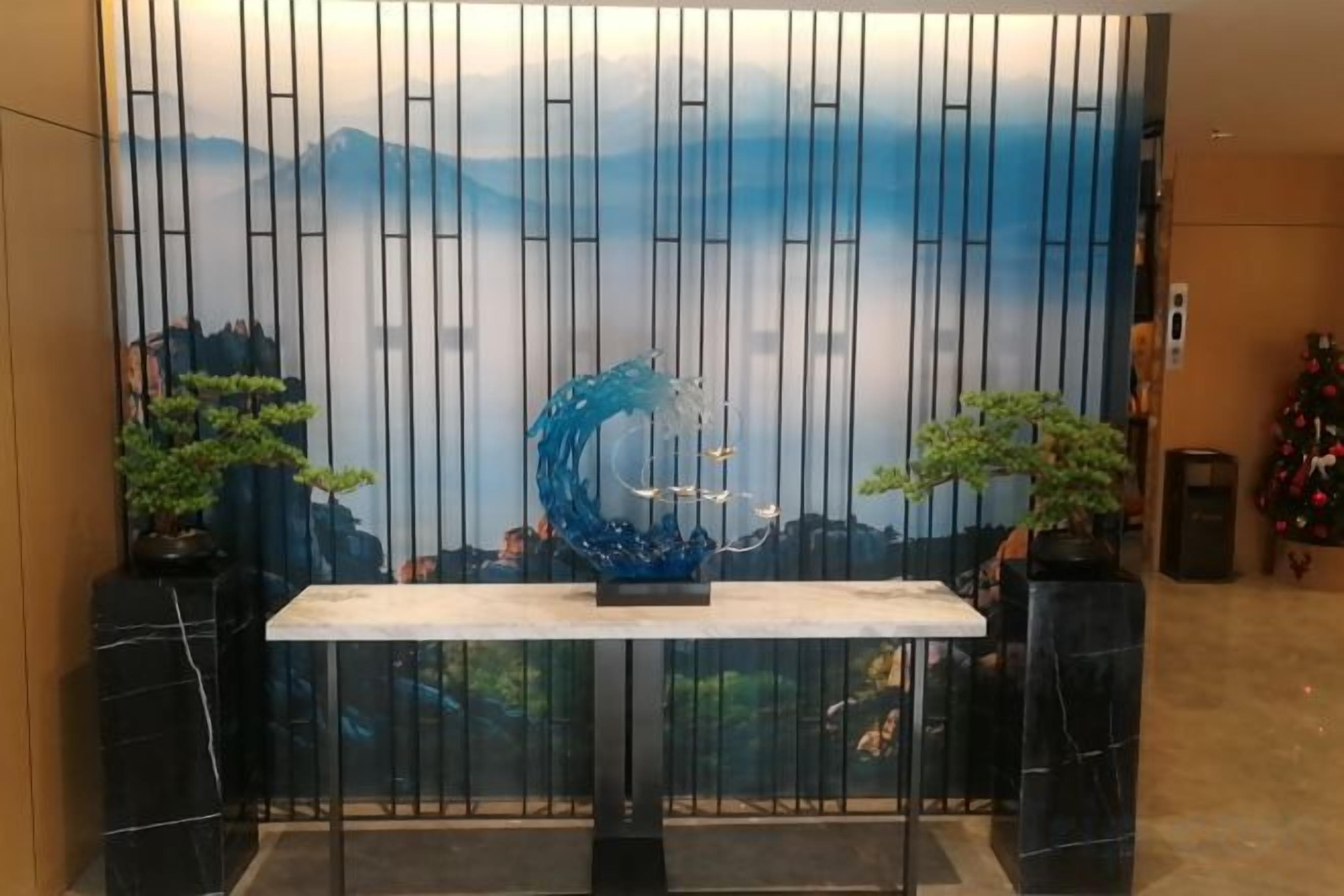 A reception area with a reception desk, a decorative wall with vertical lines, and two potted plants.