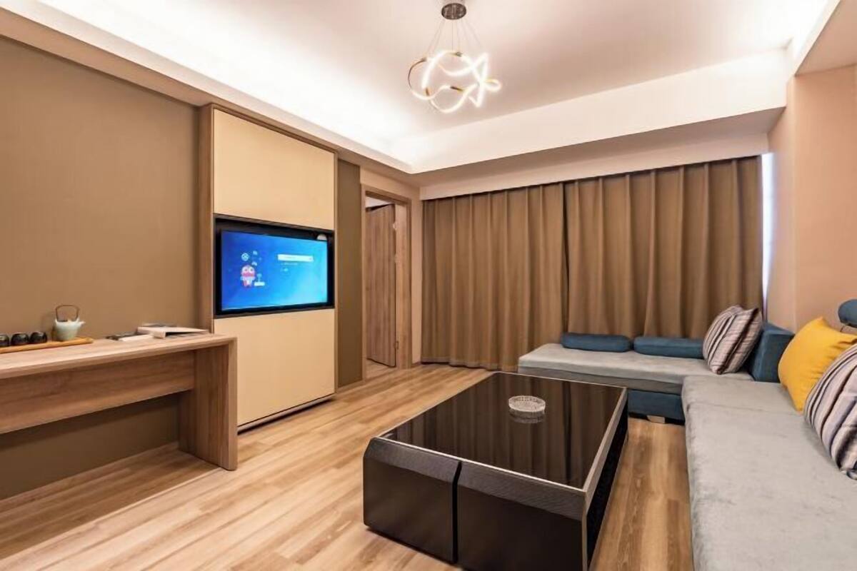 A modern living room with a flat-screen TV, a glass coffee table, a sofa, and a wooden desk.