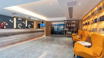 A modern lobby with a marble reception desk, a seating area with yellow chairs, and a bookshelf.