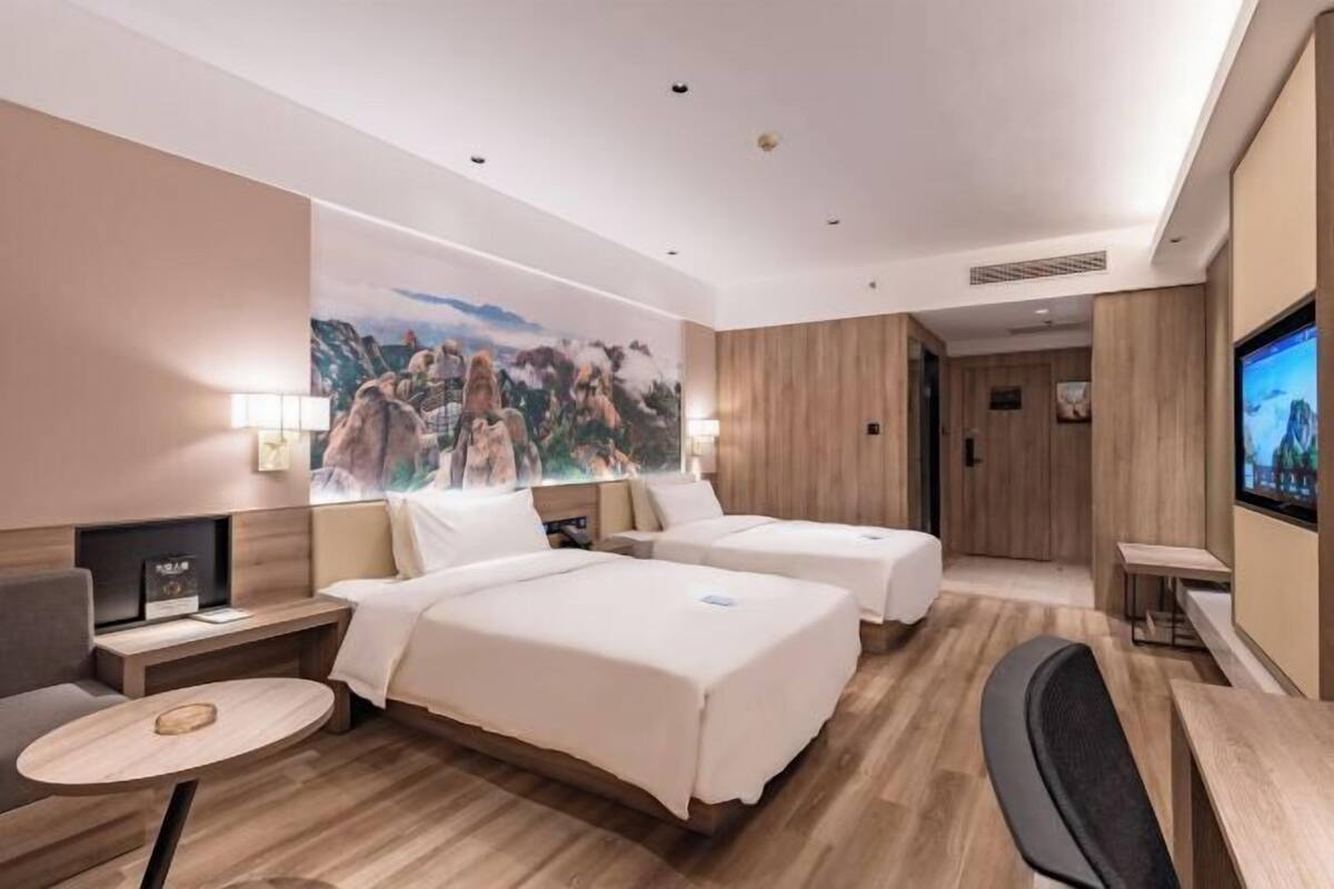 A hotel room with two beds, a television, a desk, and a wall-mounted artwork.