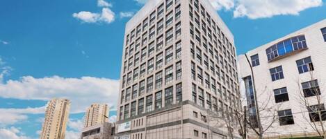 Un edificio de varios pisos con un diseño de esquina llamativo, varios espacios comerciales en la planta baja y un cielo despejado.