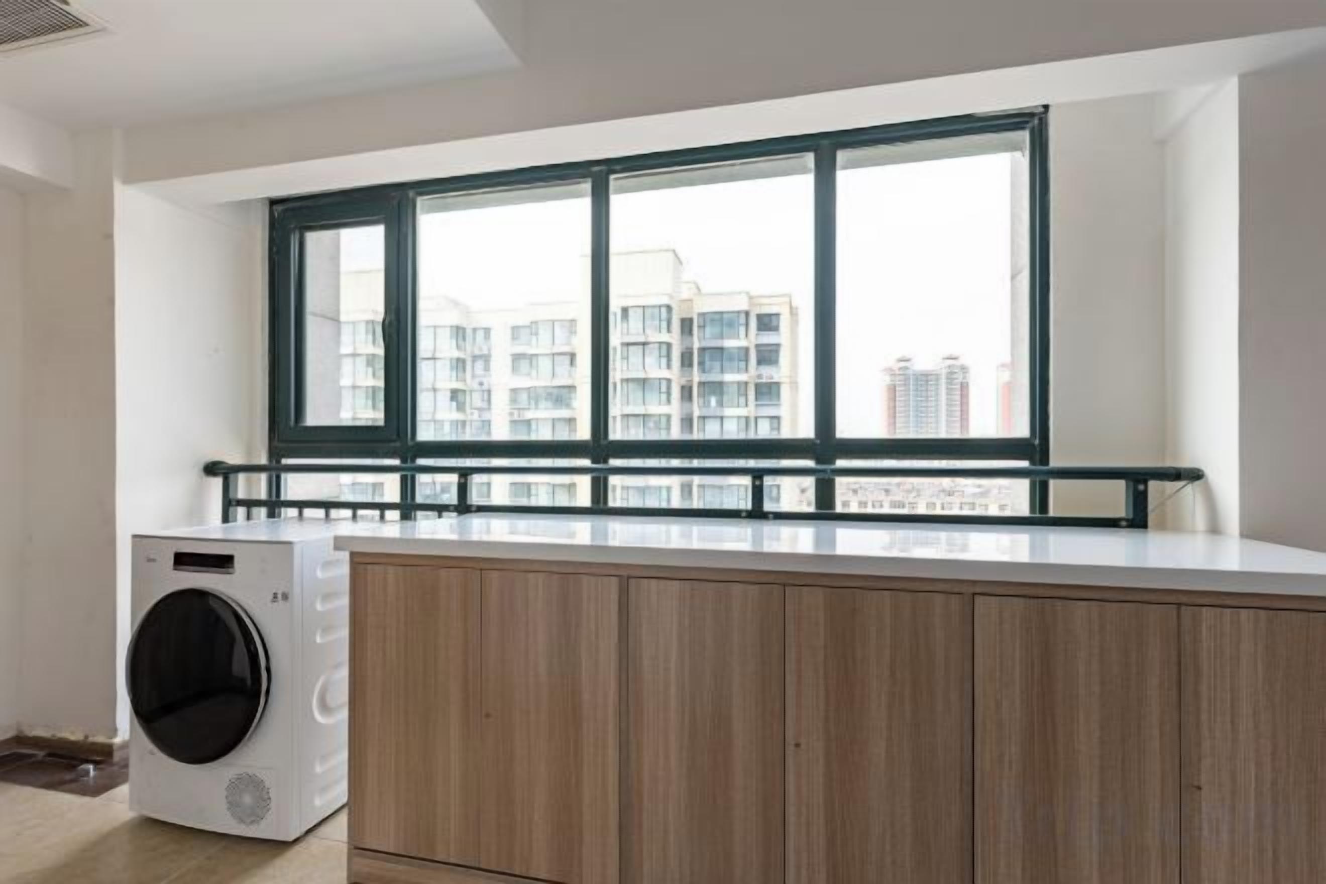 A laundry area with a washing machine, wooden cabinets, and a window with a view of buildings.