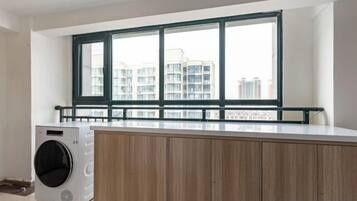 A laundry area with a washing machine, wooden cabinets, and a window with a view of buildings.
