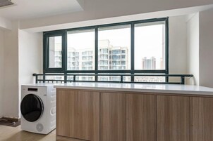A laundry area with a washing machine, wooden cabinets, and a window with a view of buildings.