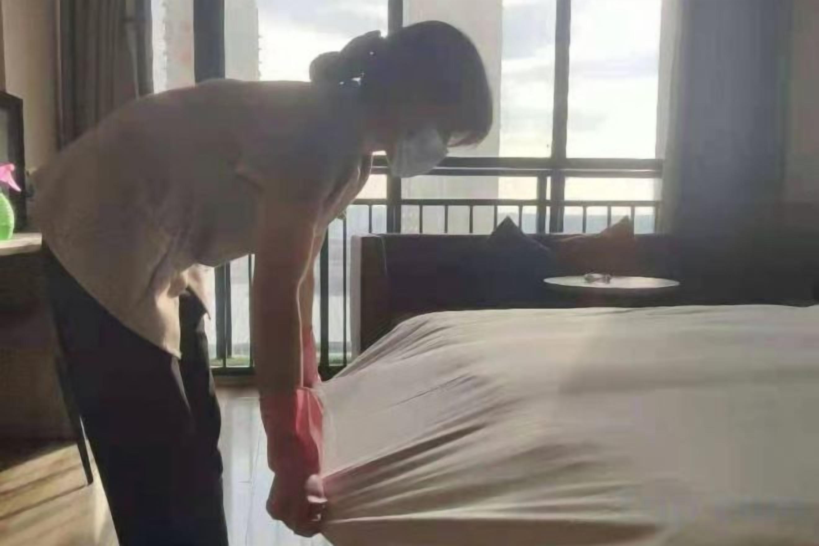Uma pessoa ajeitando uma cama em um quarto com vista para o céu pela janela.