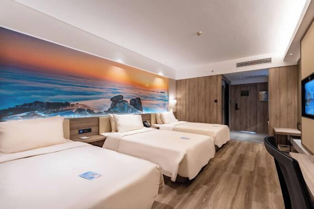 A hotel room with two beds, a TV, a painting on the wall, and a wooden floor.