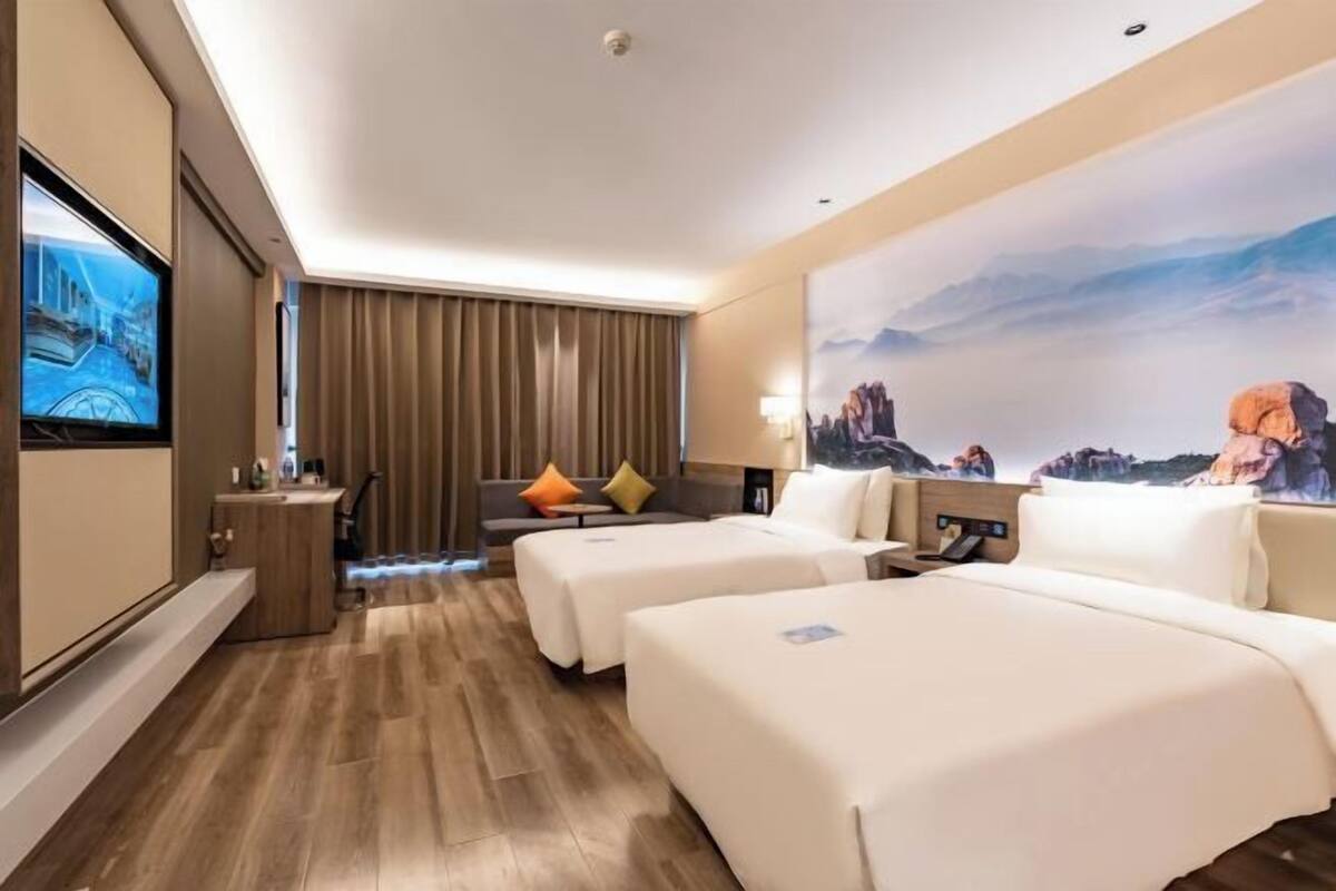 A hotel room with two beds, a TV, a desk, and a large window.