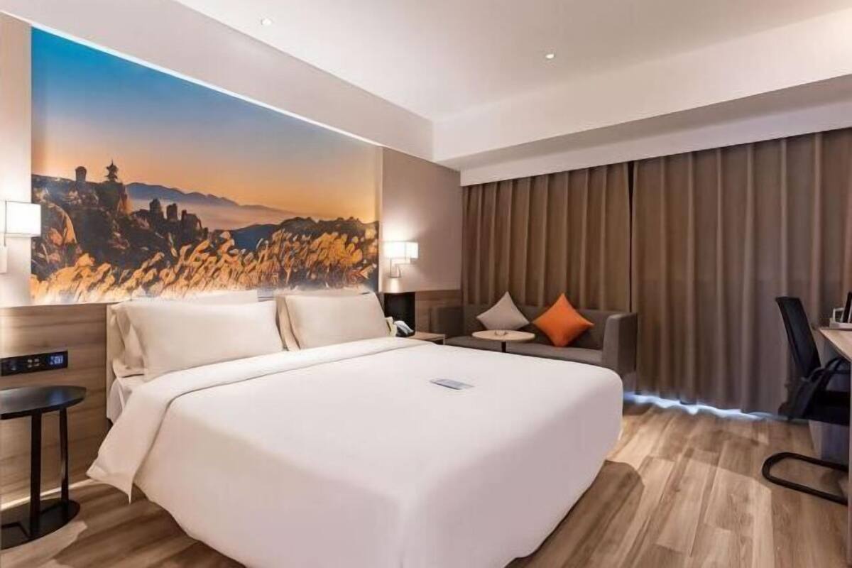 A hotel room with a large bed, a desk, a chair, a lamp, and a painting on the wall.