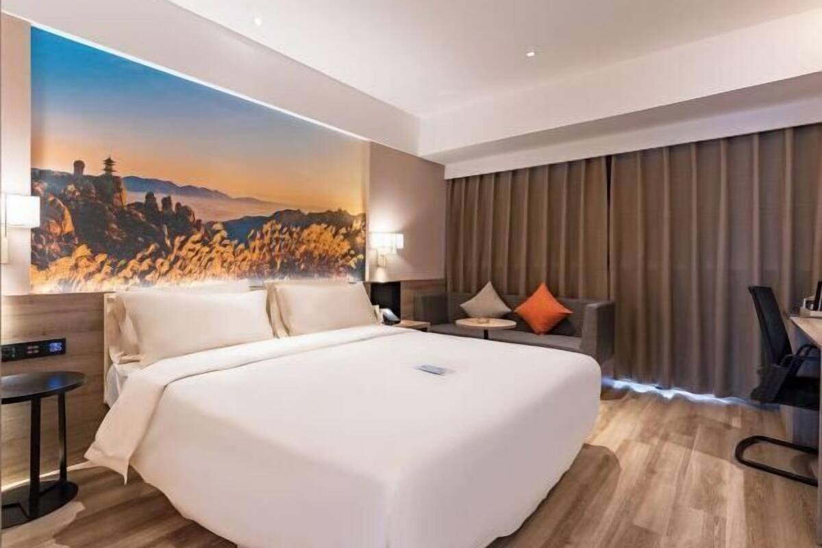 A hotel room with a large bed, a desk, a chair, a lamp, and a painting on the wall.