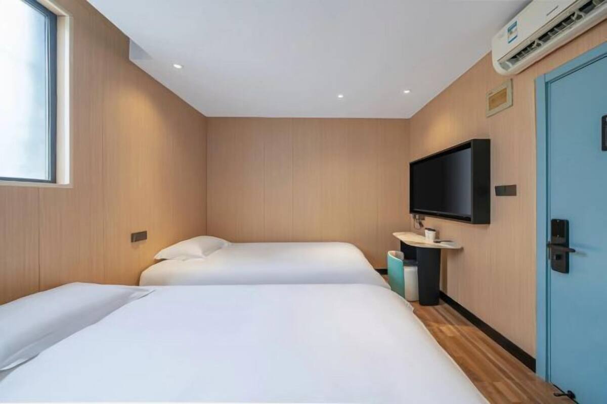 A hotel room with two beds, a TV mounted on the wall, a sink, and a door.