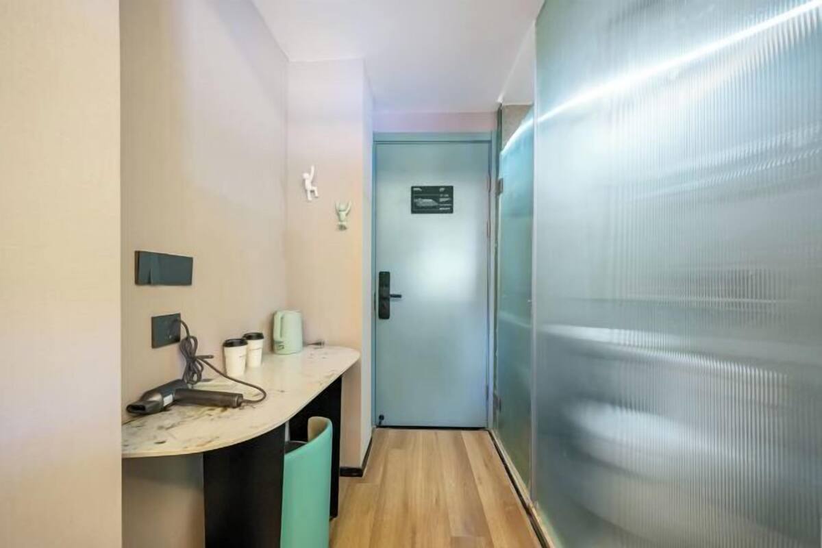 A narrow hallway with a door at the end, a small table with a kettle and a hairdryer, and a trash bin.