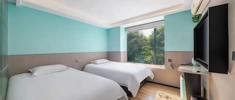 A hotel room with two beds, a TV, a window with a view of greenery, and a ceiling light.