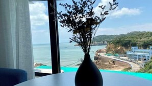 A room with a view of the sea and cliffs, a vase with dried flowers on a table, and a blue chair. - Gouqi Island Chunnuan Huakai Homestay (Shengsi)