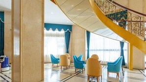 A hotel lobby with a marble floor, blue and yellow chairs, a spiral staircase, and large windows with curtains. - New Beacon International Hotel (Luotian Tashanhu Park) (Luotian County)