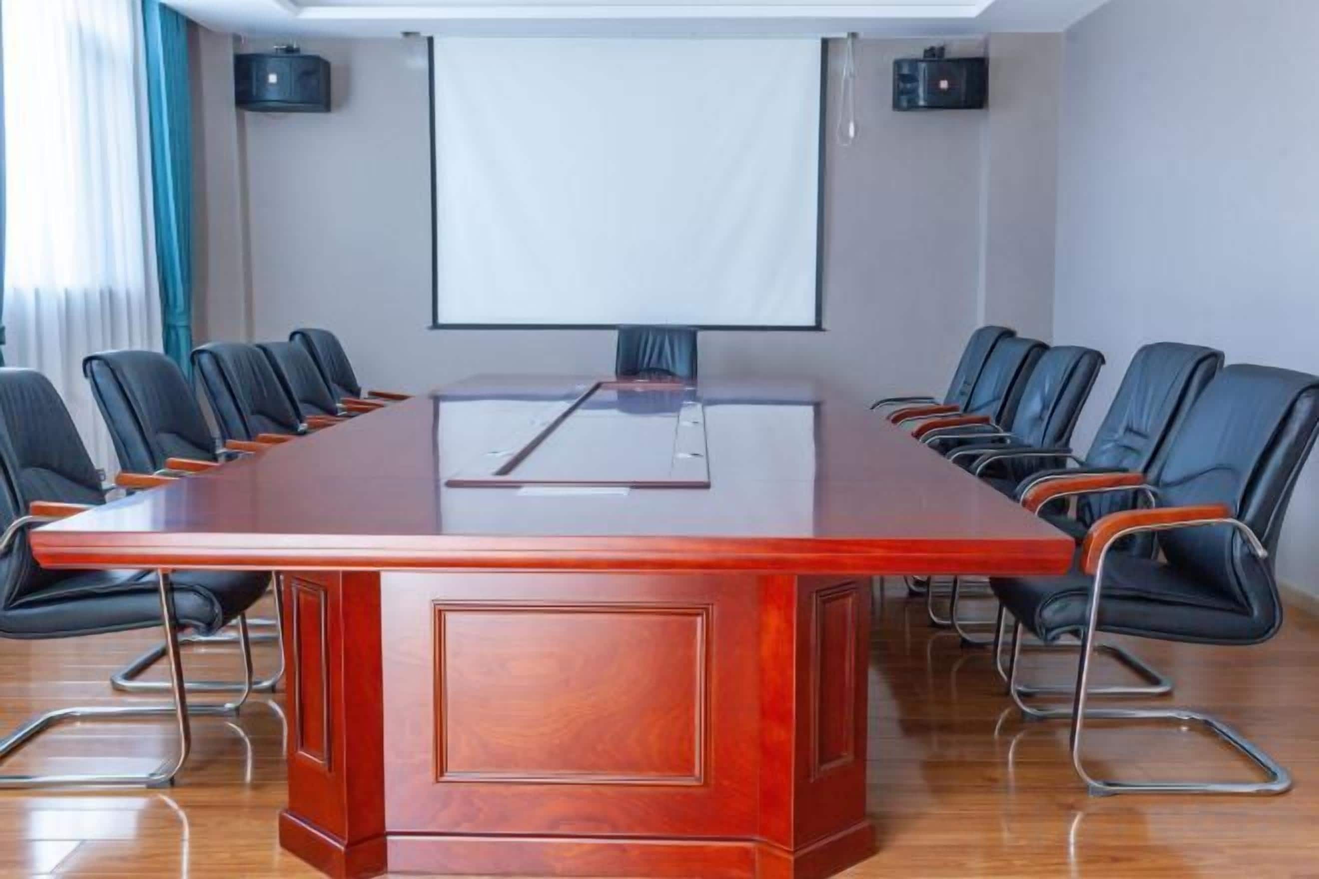 A conference room with a long table, black chairs, a projector screen, and a whiteboard.