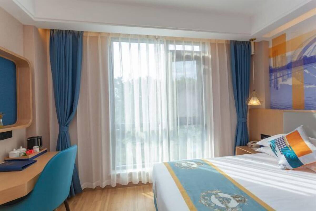 Een hotelkamer met een bed, een bureau, een stoel, een nachtkastje en een raam met gordijnen.