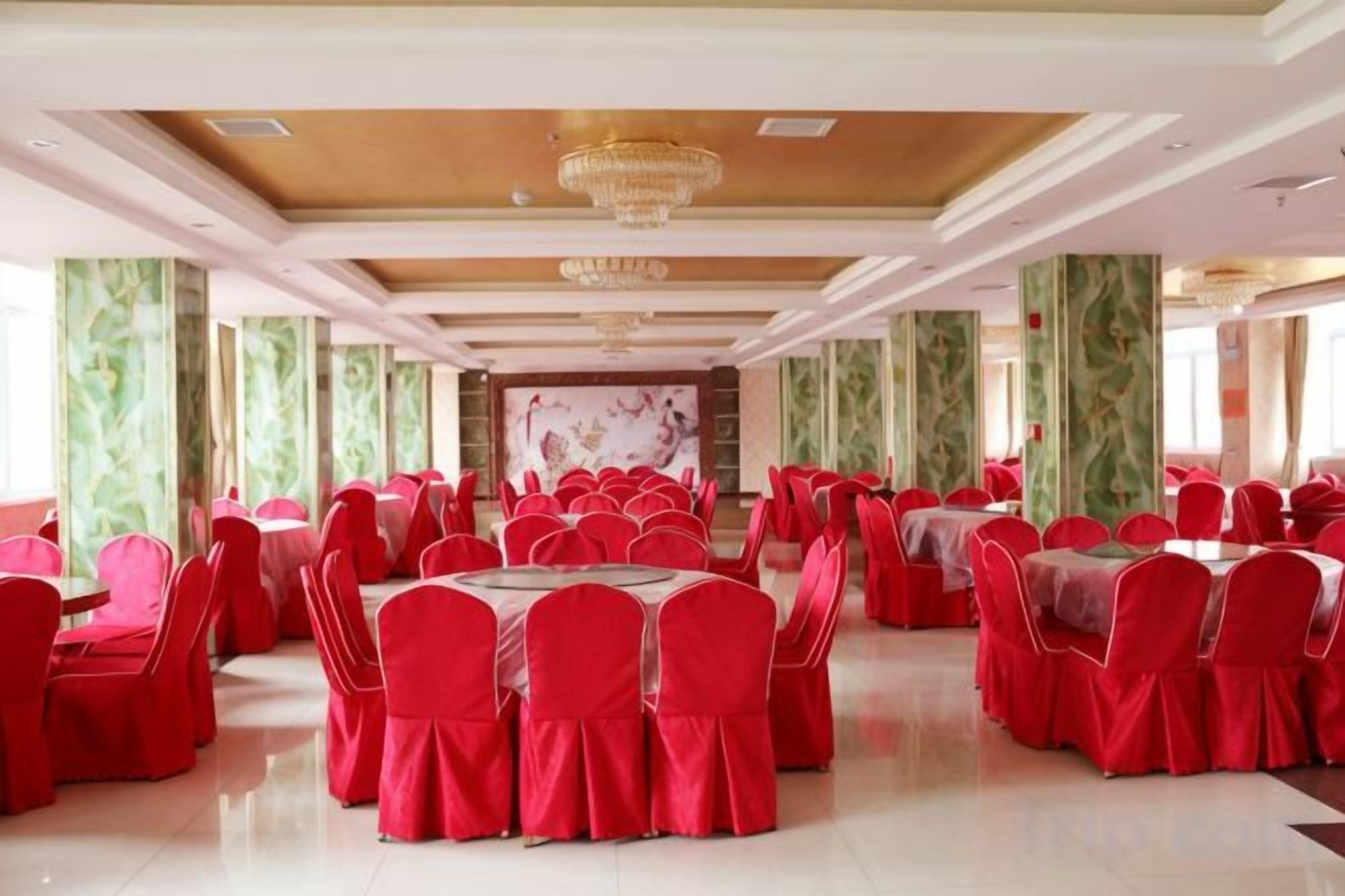 A banquet hall with round tables and chairs, a chandelier, and green patterned wallpaper.