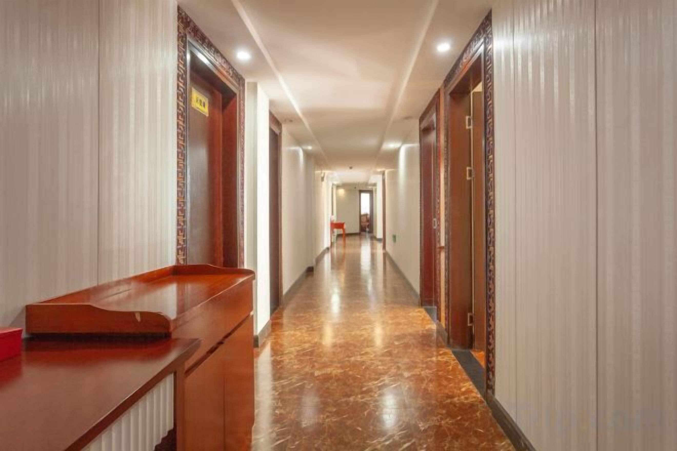A hotel hallway with a reception desk, doors, and a marble floor.