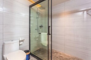 A modern bathroom with a glass-enclosed shower, a toilet, and a trash bin.