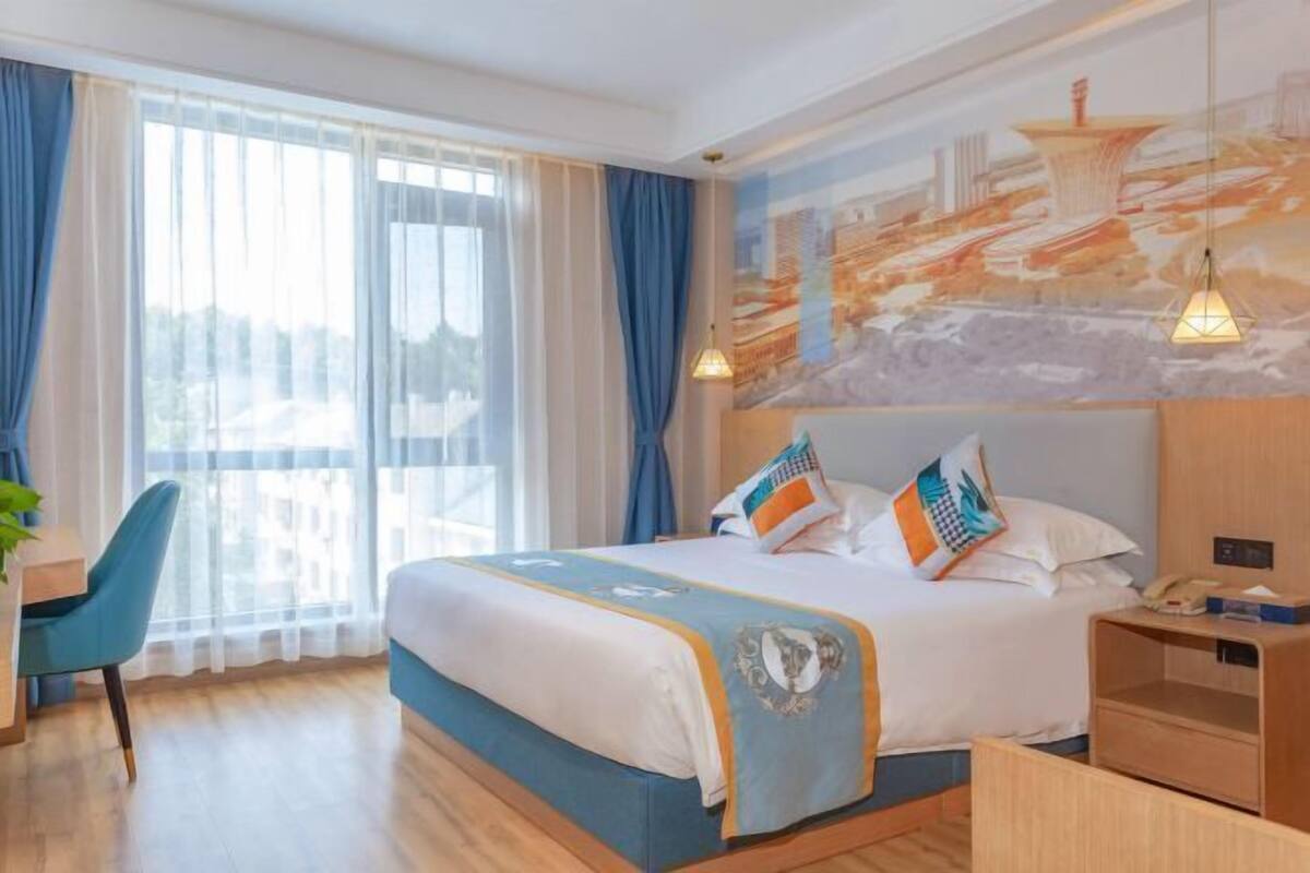 Hotelkamer met een bed, bureau, stoel, nachtkastje en een groot raam met gordijnen.