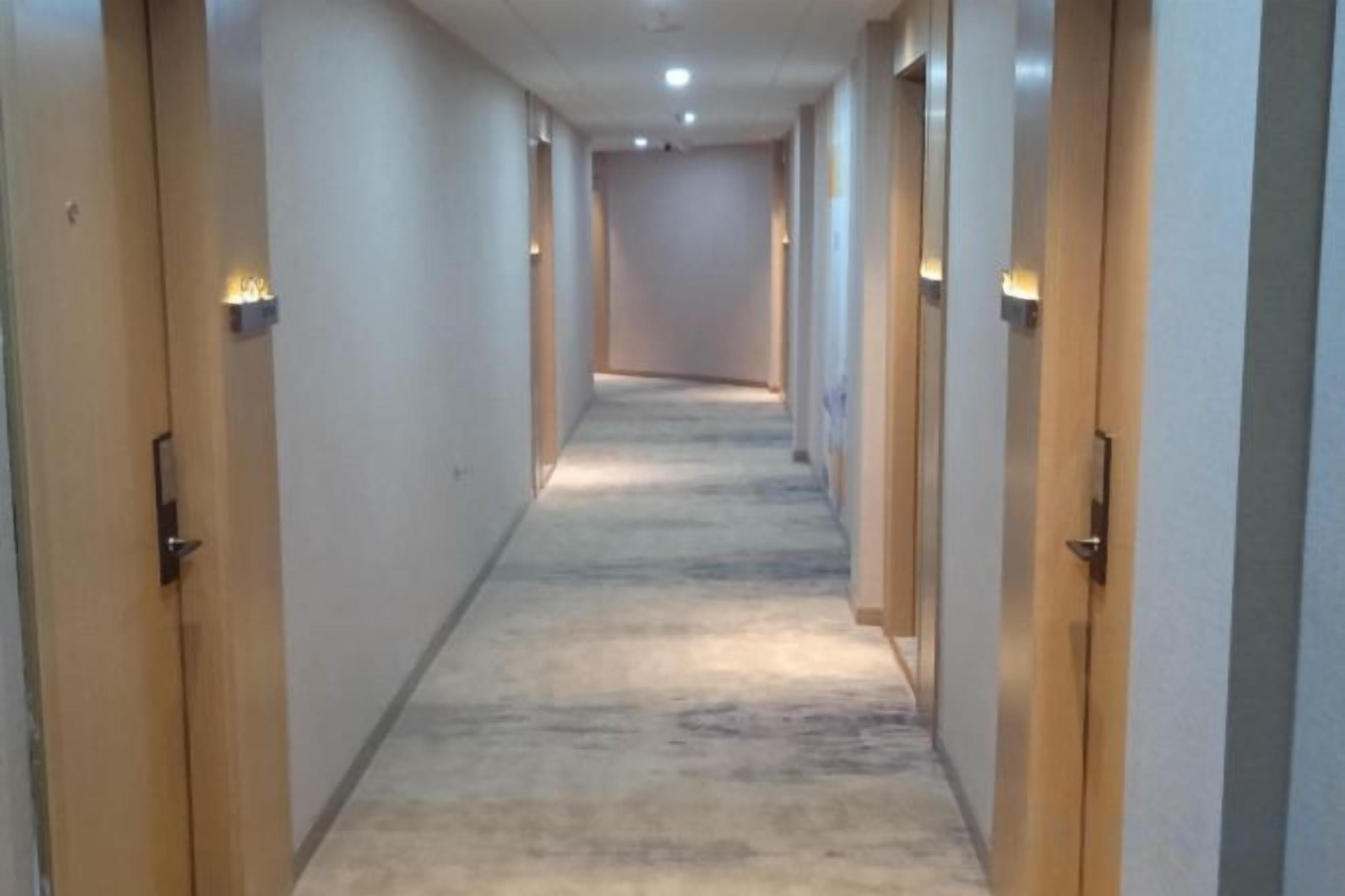 A long, narrow hallway with doors on both sides, carpeted floor, and recessed lighting.