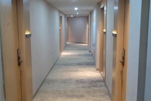 Un pasillo largo y estrecho con puertas a ambos lados, piso alfombrado e iluminación empotrada.