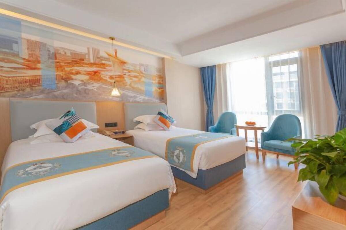 Een hotelkamer met twee bedden, een klein tafeltje, een stoel en een groot raam met gordijnen.