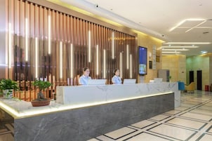 Un mostrador de recepción con cubierta de mármol, listones de madera verticales y dos recepcionistas.