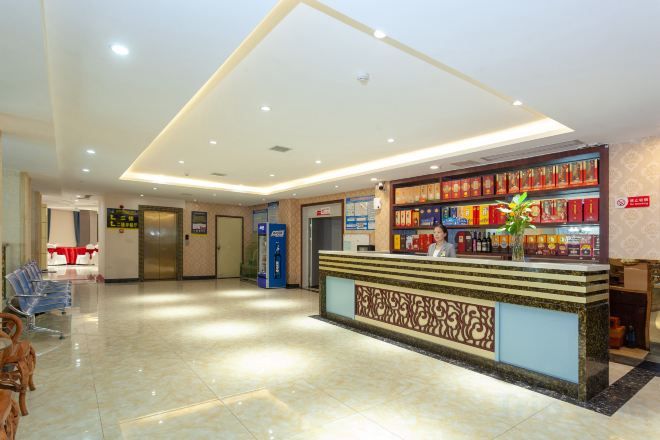 A hotel reception area with a reception desk, a plant, and a wall with bookshelves.