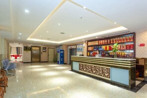Zona de recepción de hotel con mostrador, una planta y una pared con estanterías.