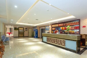 Zona de recepción de hotel con mostrador, una planta y una pared con estanterías.