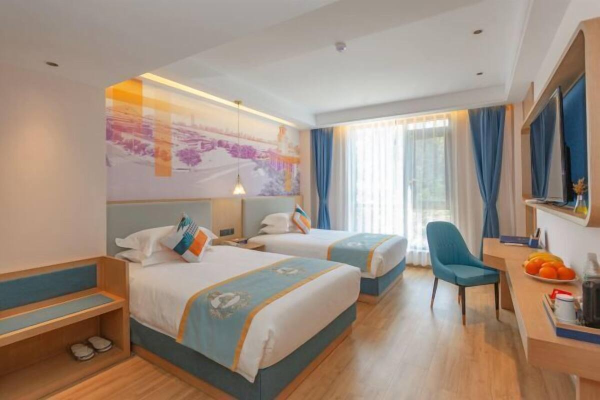 Een hotelkamer met twee bedden, een bureau met stoel, een televisie en een raam met gordijnen.
