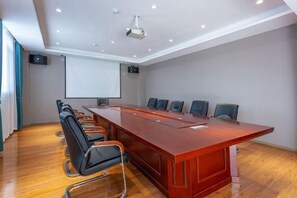 Un salón de conferencias con una larga mesa, sillas, una pantalla de proyector y una pizarra.