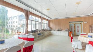 A spacious room with tables and chairs, a kitchen area, and large windows.