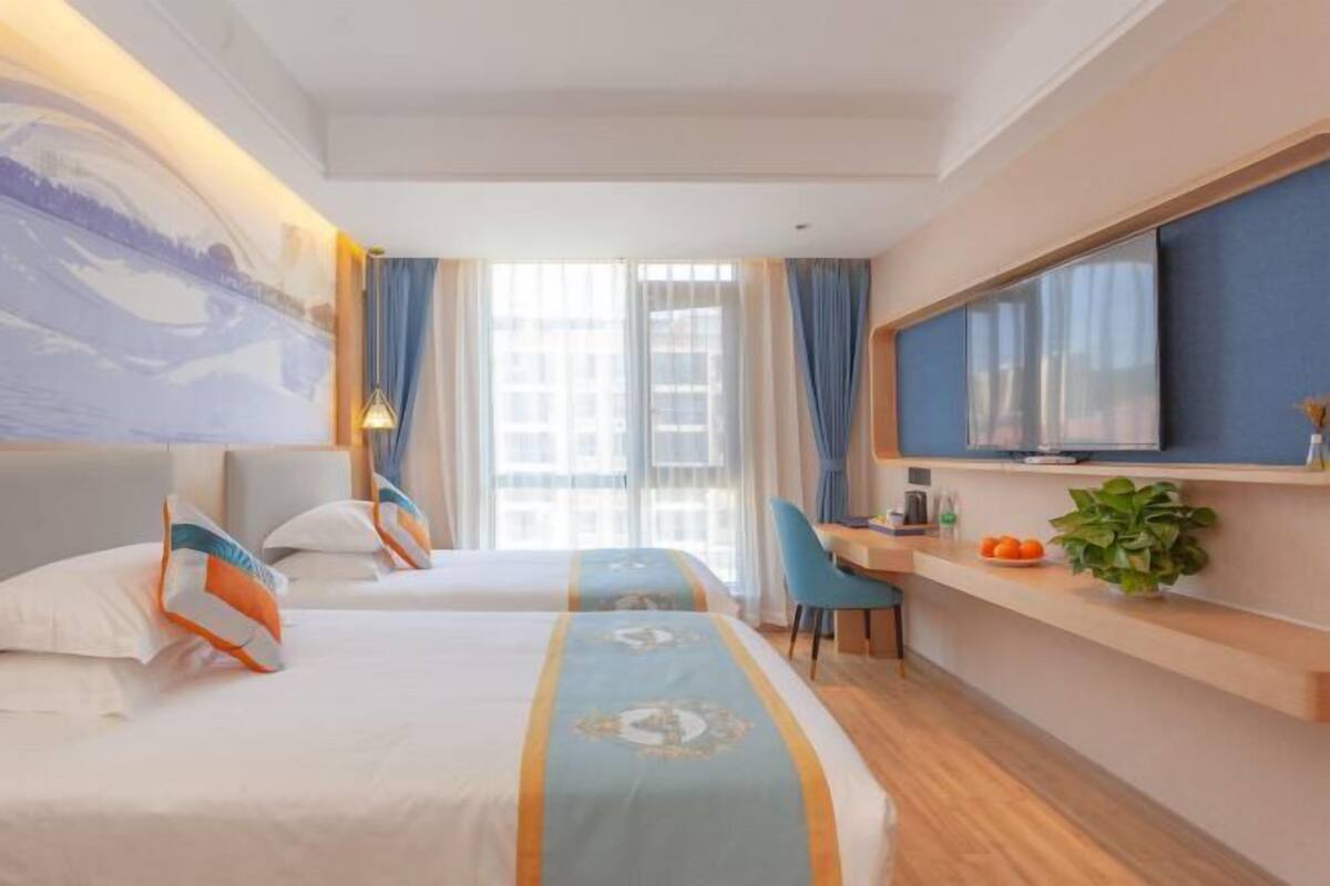 Een hotelkamer met twee bedden, een bureau, een televisie en een groot raam met gordijnen.