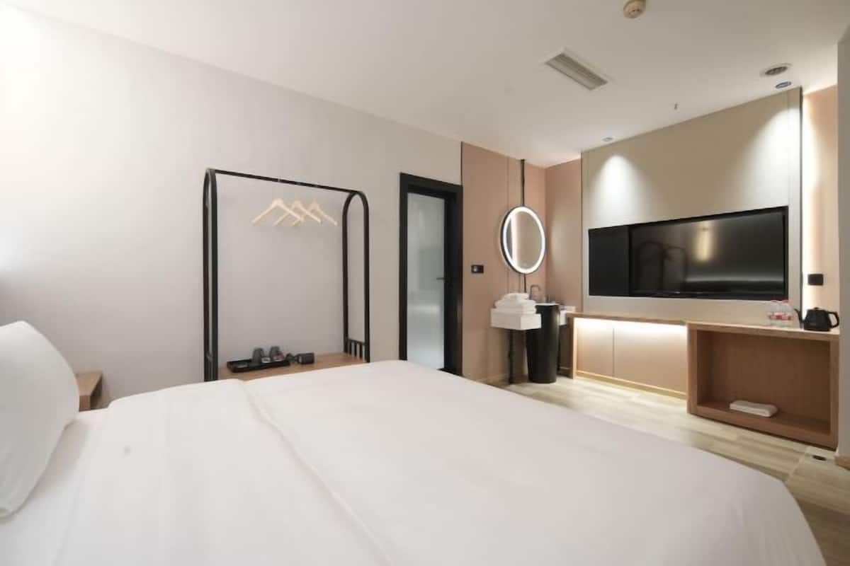 A modern hotel room with a large bed, a TV mounted on the wall, a mirror, and a small seating area with a table and chairs.