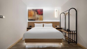 Ett modernt hotellrum med en stor säng, ett sängbord, ett litet bord och ett konstverk som hänger på väggen.