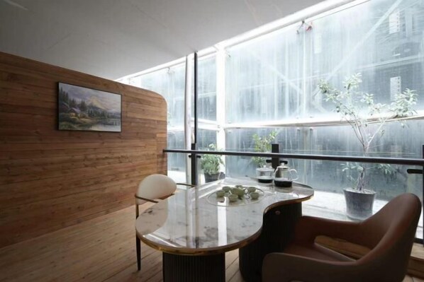 A room with a wooden wall, a painting, a round table with chairs, and a view through large windows.