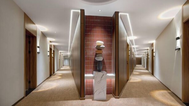 En modern hotellkorridor med en central konstinstallation, trädörrar och infälld belysning.