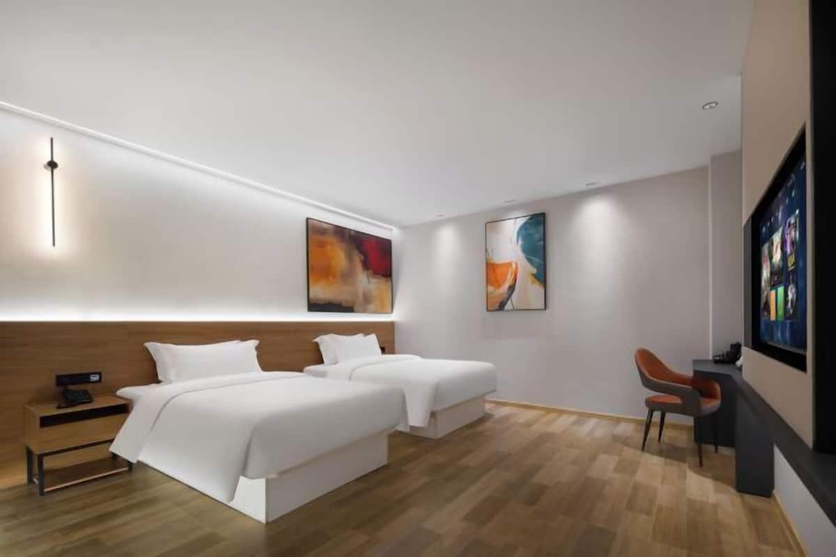 A modern hotel room with two beds, a desk, and artwork on the walls.