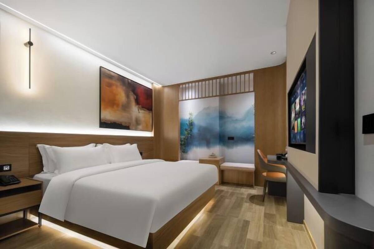 A modern hotel room with a large bed, a bedside table, a TV, and artwork on the walls.