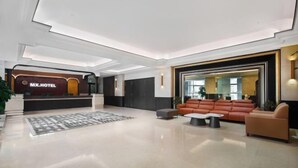 En rymlig entréhall med en receptionsdisk märkt "MX.HOTEL", ett stort område med sittplatser och soffor samt en modern takdesign.