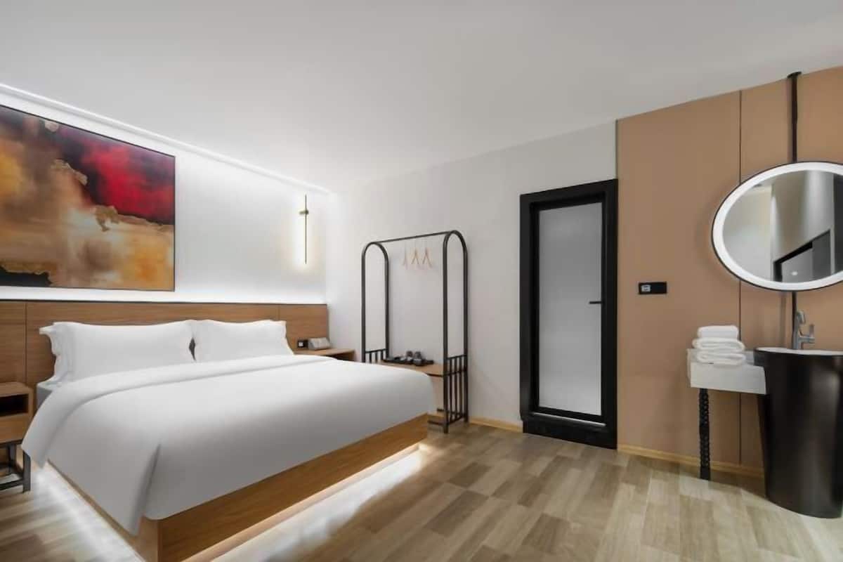 A modern hotel room with a large bed, a bedside table, a wall-mounted TV, a mirror, and a door.