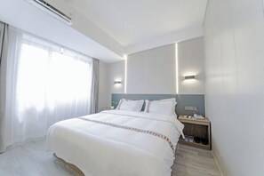 Una habitación de hotel con una cama grande, mesitas de noche, un ventanal con cortinas y un equipo de aire acondicionado.