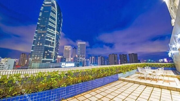A rooftop terrace with a view of a city skyline at night, featuring modern buildings and a clear sky.