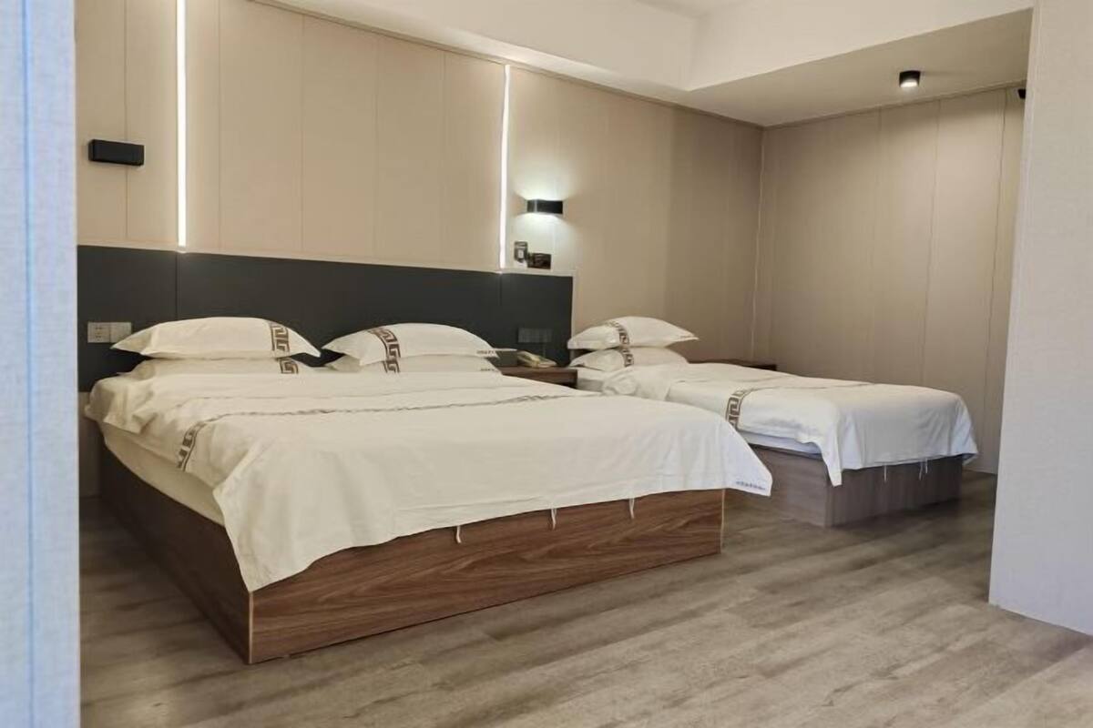 Une chambre d’hôtel avec deux lits, chacun doté d’une tête de lit en bois et de linge de lit blanc. Un luminaire est fixé au mur au-dessus des lits, et une petite table se trouve entre les deux.