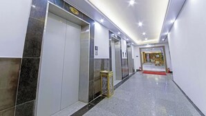 A hallway with three elevators, each marked with a number. The hallway has a polished floor and is well-lit with ceiling lights.